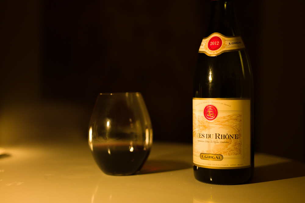 Candle-lit photo of stemless wine glass and a bottle of E. Guigal Cotes du Rhone Red 2012