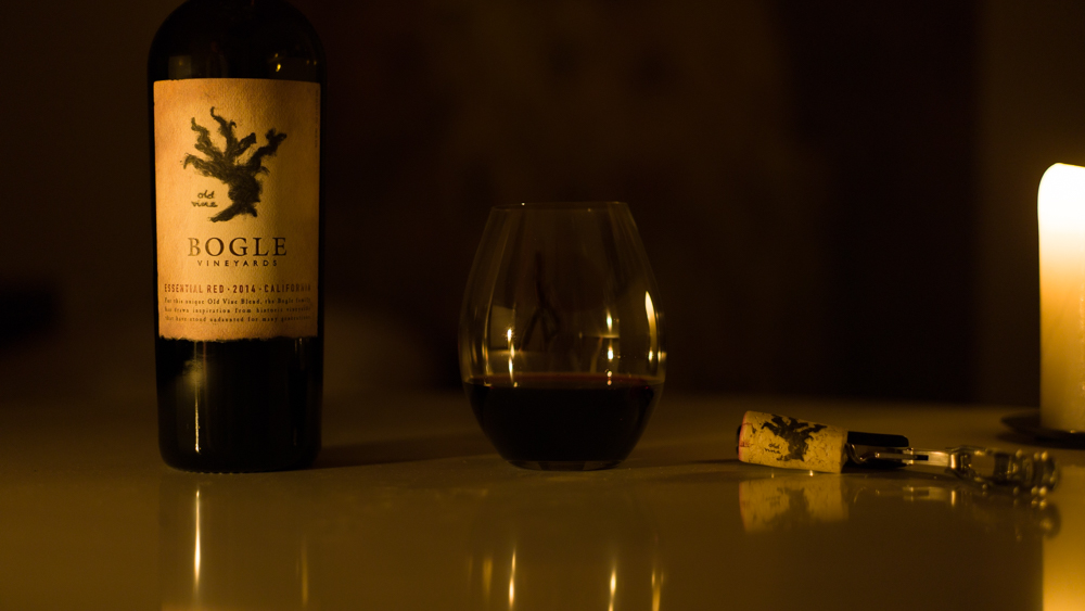 Candlelight photo of bottle of Bogle Essential Red wine, with a glass and the cork.