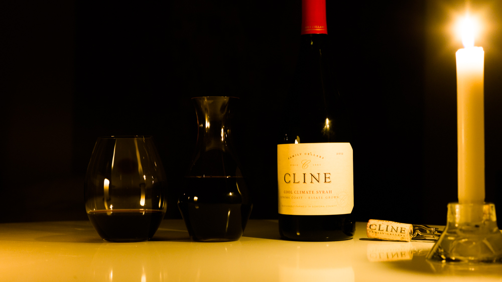 Candlelight photograph of wine bottle, carafe, glass, and cork.